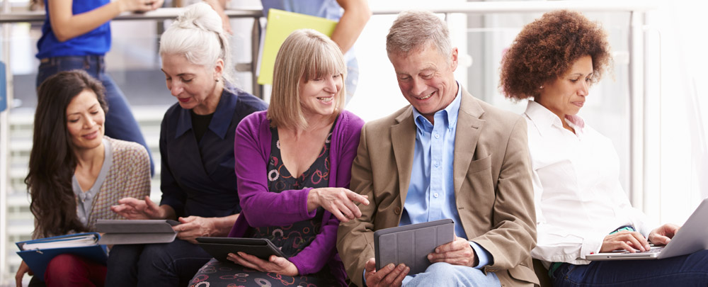 group of people talking in smaller groups, on phones or laptops, smiling