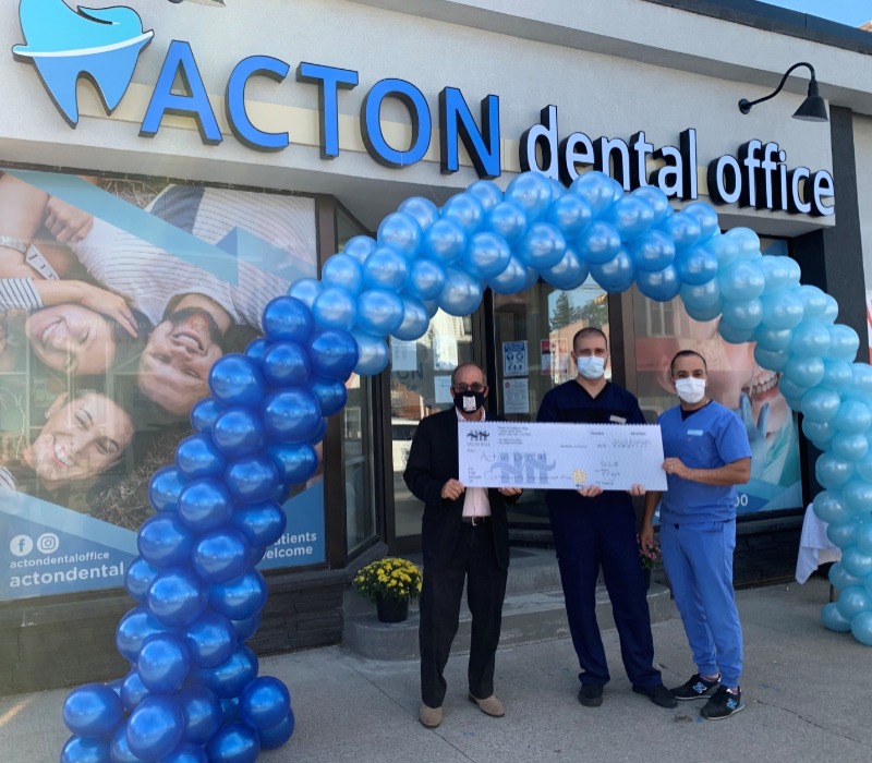 Owners and Mayor holding cheque in front of Acton Dental Office