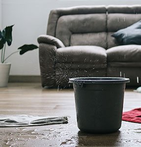 A bucket of water catching dripping water from above in a living room