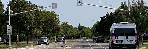 ActiVan parked on the right side of the road and a man in front of it walking through a cross walk