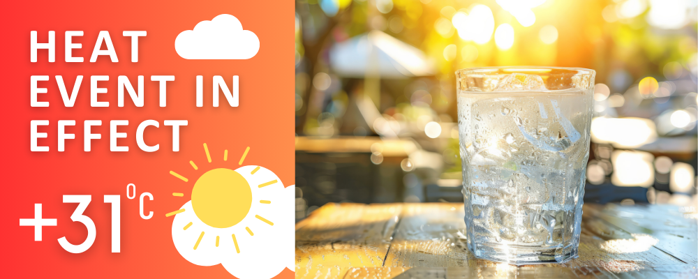 The wording "Heat event in effect, +31 celsius" with a glass of ice water on a restaurant patio at sunset