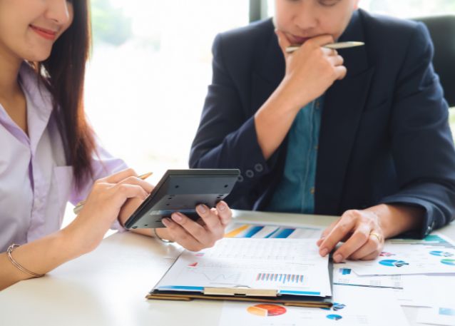 A man and a woman reviewing various paper with charts and graphs holding a calculator